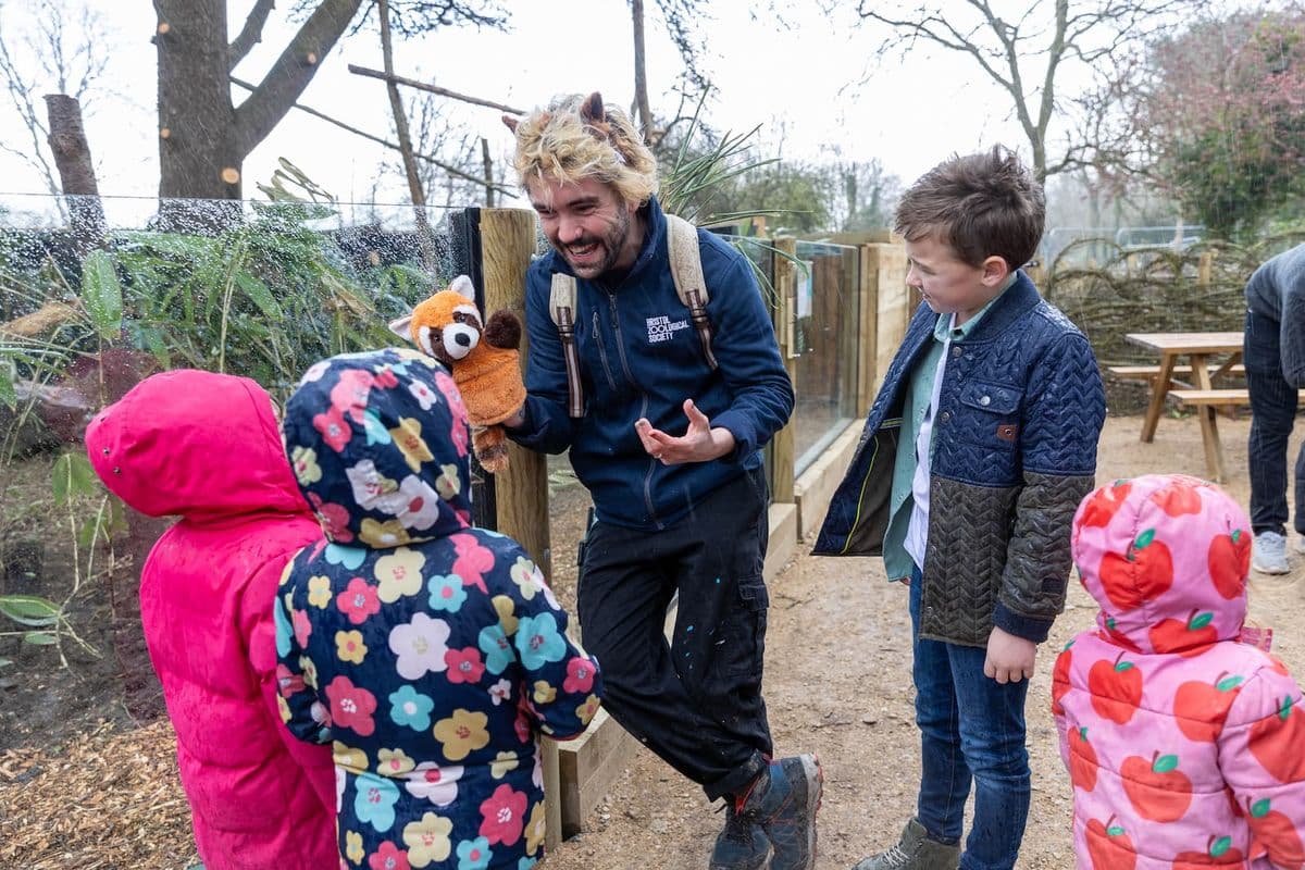 A Bristol Zoo Project staff member talks to a group of children while holding a red panda puppet