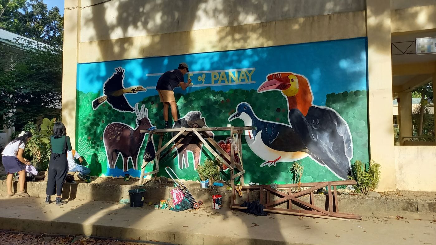 Members of the community painting a mural on a large wall, it features threatened animals from the Philippines